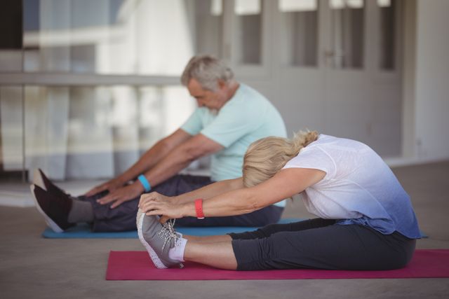 Senior couple stretching together on yoga mats at home, promoting a healthy and active lifestyle. Ideal for use in articles or advertisements about senior fitness, home workouts, wellness programs for the elderly, and maintaining physical health during retirement.