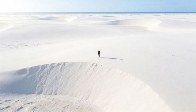 Solitary figure standing on vast white dunes casting long shadow and leaving footprints