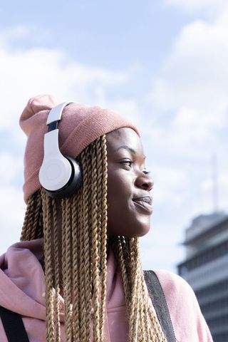 African American woman wearing beanie and headphones listening to music outdoors in urban daylight