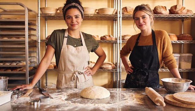 Two Bakers Kneading Sourdough Dough on Steel Table in Rustic Artisan Bakery for Small Business