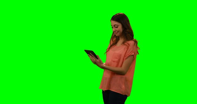 Young woman casually using a tablet with a green screen background. Suitable for tech demonstrations, promotional content, educational videos, advertising, or social media posts, as green screen allows easy addition of custom backgrounds.