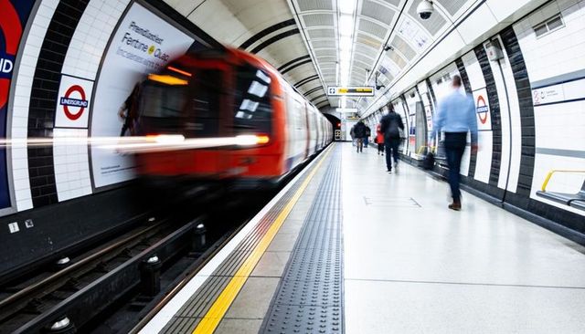 Rush-hour underground platform with speeding red train and blurred commuters walking