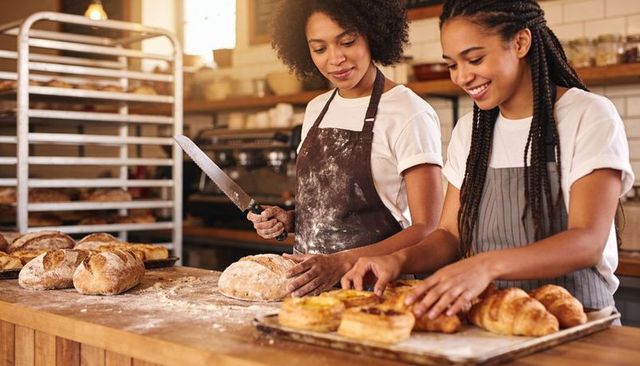 Artisan bakers slicing loaf and arranging pastries on wood counter in cozy bakery