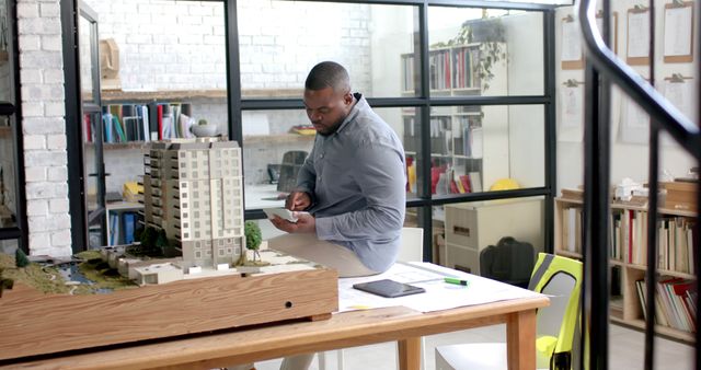 Architect reviewing building model in modern office setting. Suitable for topics on architecture, creative industries, professional work environment, design process. Ideal for articles, websites, or advertisements related to architectural firms, modern workspaces, and creative professions.