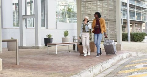 Diverse travelers walking with suitcases and coffee at urban transit drop-off