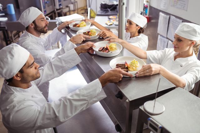 Chefs passing ready food to waiter  at order station in commercial kitchen