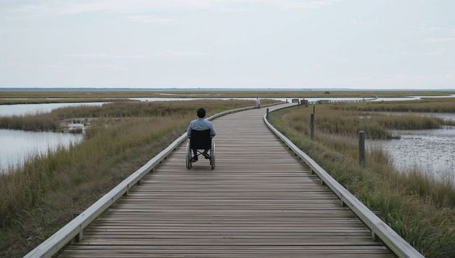 Man in wheelchair rolling along wooden boardwalk through coastal marsh and tidal pools