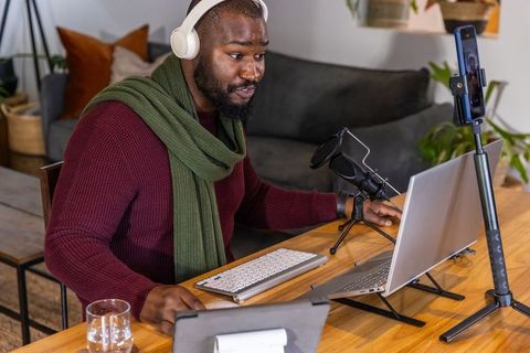Recording podcast from home desk with laptop microphone headphones and smartphone
