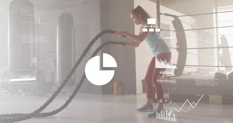 Female athlete swinging battle ropes in industrial gym with fitness hud graphics