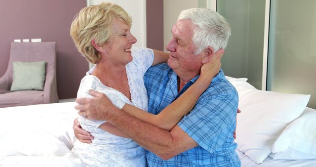 Happy elderly couple embracing with smiles in cozy bedroom. Perfect for projects on senior love, companionship, retirement, happy relationships, and elderly lifestyle. Excellent for advertisements, blogs, and articles focusing on aging, family, and cozy home settings.