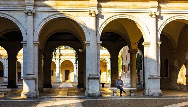Man sitting on stone bench soaking up golden hour sunlight under historic arcades