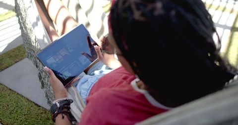 Young woman relaxing in hammock while browsing tablet