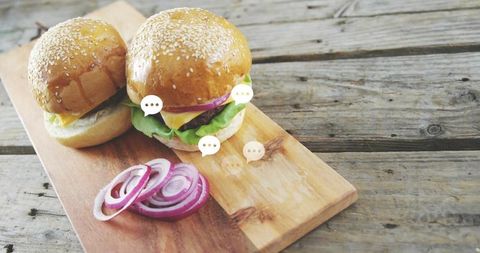 Two sesame brioche sliders resting on rustic wooden board with cheese and red onion