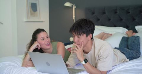 Young couple relaxing on bed watching laptop and checking smartwatch in cozy bedroom
