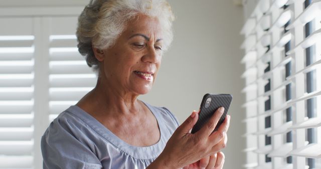 African american senior woman using smartphone and looking out of the window at home. retirement senior lifestyle living in quarantine lockdown concept