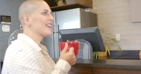 Bald woman holding red mug at cafe counter with pos tablet, casual conversation mood