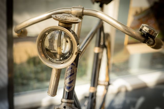 This image captures a detailed close-up of a vintage bicycle's headlight and handlebars, showcasing antique metal craftsmanship and old-fashioned design. Perfect for use in themes related to transportation history, nostalgic travel, or retro decor.