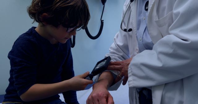 Young boy using a magnifying glass to examine doctor's arm in medical office. Doctor wearing stethoscope and white coat. Useful for illustrating pediatric care, educational activities in healthcare environments, or promoting medical learning experiences.