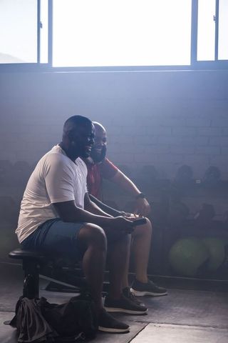 African american friends resting at gym bench checking smartphone laughing after workout