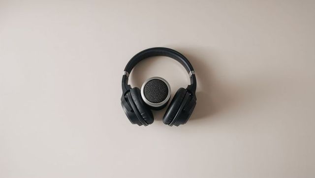 Framing black over-ear headphones around silver speaker on pale beige minimal background