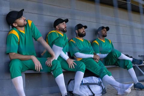 Baseball players sitting in dugout wearing green yellow uniforms during game break