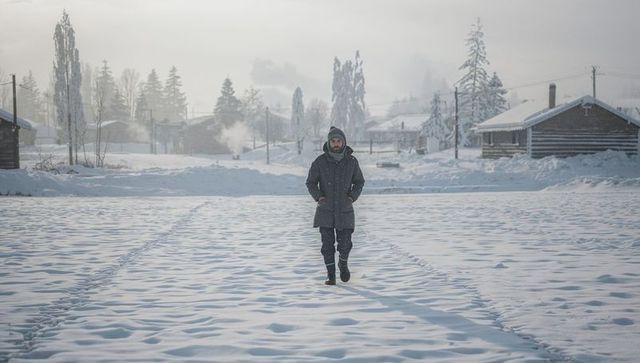 Solitary man walking through snowfield toward camera wearing parka and winter boots