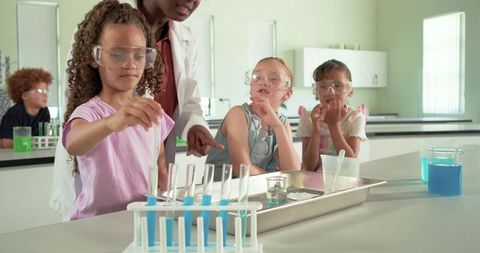Young students conducting colorful chemistry experiment with teacher in bright science lab