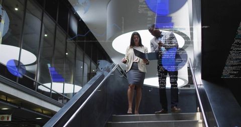 Business leaders reviewing digital data on laptop while descending modern atrium stairs