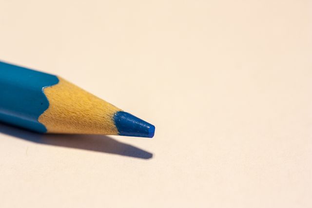 Close-up view of a blue pencil laid on a white surface with its tip sharpened and ready for use. This image can be used for themes related to art and education, ideal for school projects, stationery branding, or creative design blogs.
