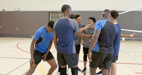 Multiracial male volleyball team gathering in gymnasium celebrating teamwork and unity