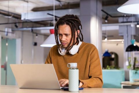 Young African American man concentrating on laptop in modern open-plan coworking space
