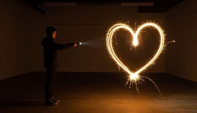 Woman in beanie holding flashlight creating sparkler heart with long exposure glow