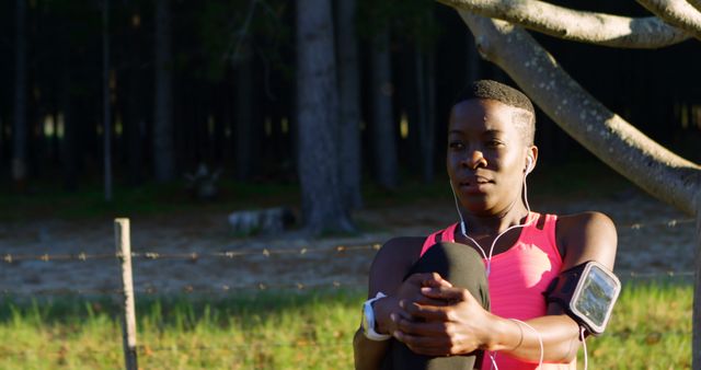 Outdoor exercise scene featuring young female jogger sitting relaxed in park with earphones. Great for fitness, lifestyle, and health-related content.