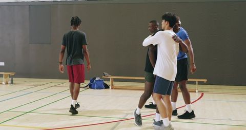 Multiracial teammates exchanging high-fives and handshakes after basketball play in gym