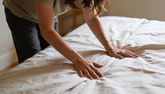 Woman smoothing duvet and making bed in natural light cozy bedroom morning routine