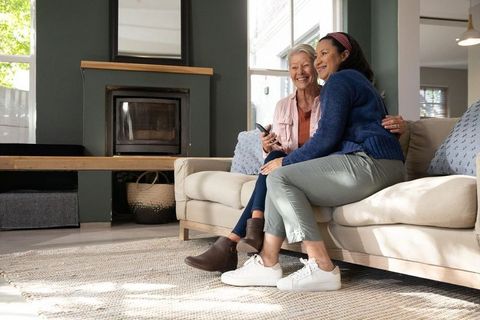 Mature women laughing and watching tv on beige sofa in bright cozy living room