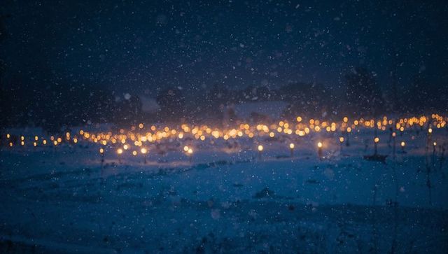 Glowing lanterns lighting snowy field at night with falling snow and warm bokeh