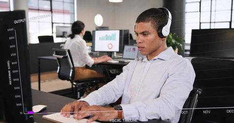 Focused data analyst typing with headphones in modern open office with financial charts