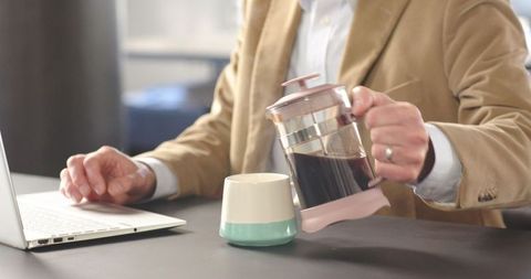 Businessman preparing coffee with french press at office desk