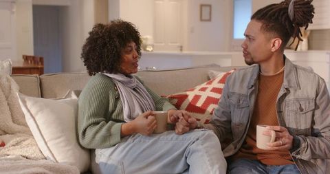 African american couple holding hands, sipping mugs and sharing warm conversation on couch