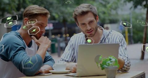 Two colleagues collaborating on laptop at outdoor cafe with eco icons, coffee cup and plant