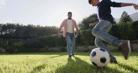 Father and Son Playing Soccer in Sunlit Backyard