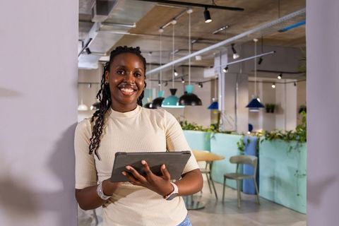 African american woman leaning against column holding tablet in modern coworking space