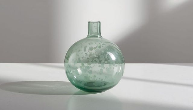 Seafoam green round glass vase with narrow neck on sunlit white surface