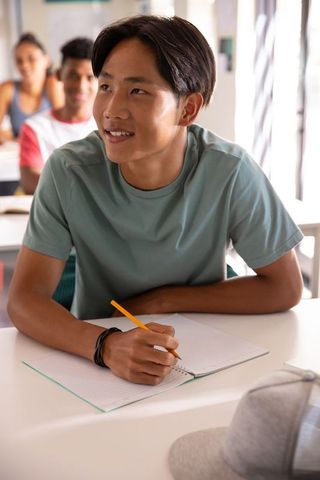 Asian teen studying in bright classroom writing notes with pencil