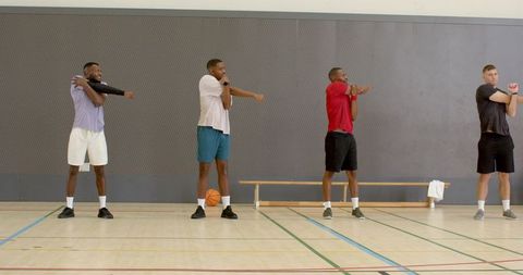 Basketball players warming up with arm stretches on indoor gym court during team training