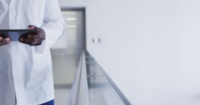 Medical professional in lab coat holding a tablet in a modern hospital hallway. Perfect for illustrating themes of healthcare innovation, modern medical practices, and the use of technology in clinical settings. Ideal for promotional materials, healthcare technology articles, medical industry websites, and educational content.