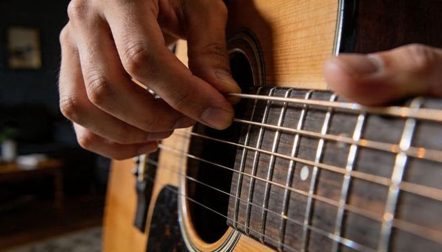 Closeup Hands Plucking Acoustic Guitar Strings Over Soundhole and Fretboard