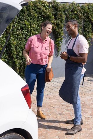 Small business owner chatting with customer beside open car trunk on sunlit courtyard