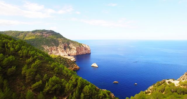 Aerial view of a coastal Mediterranean landscape showcasing lush green hills, rocky cliffs, and deep blue sea. Ideal for travel magazines, tourism websites, and promotional material for holiday destinations. Perfect for themes related to nature, tranquility, and escape from urban life.